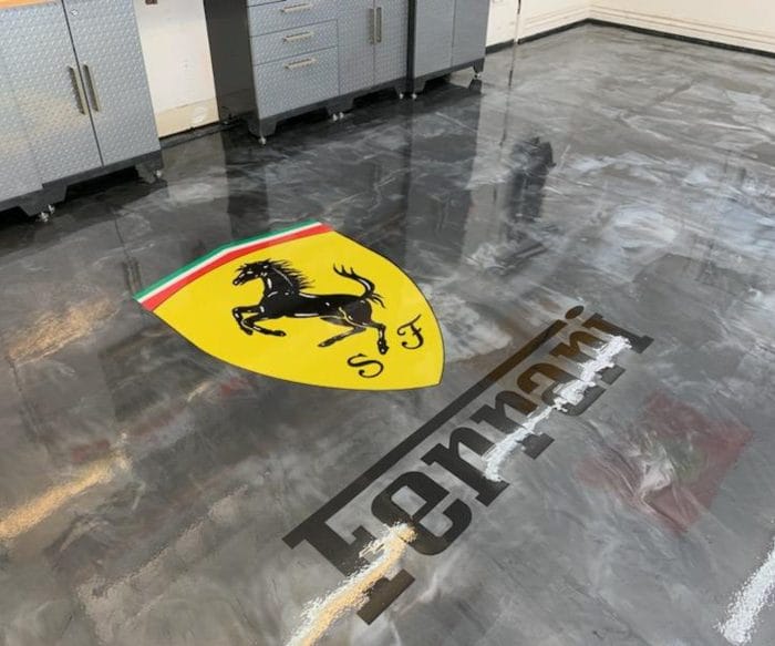 Custom sealed vinyl inlay epoxy floor featuring a bold graphic logo in a Southwest Florida showroom garage