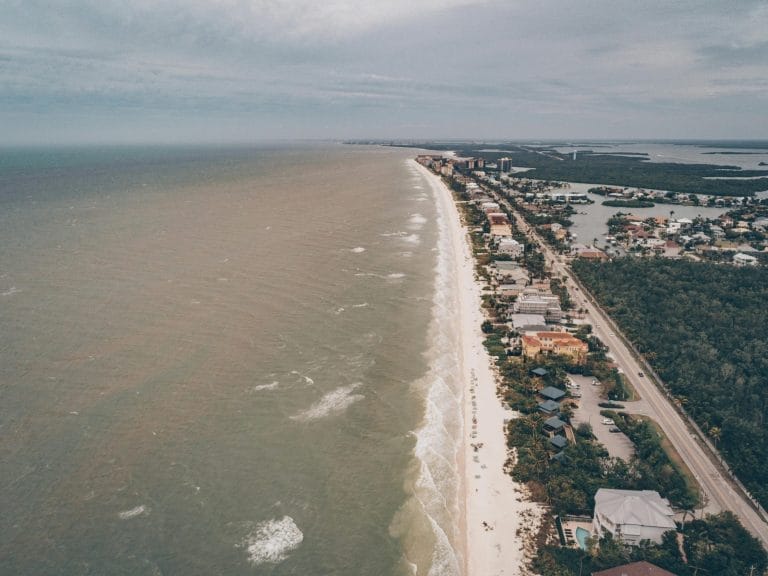 Peaceful beach in Naples, Florida with white sand, gentle waves, and a calming coastal atmosphere under a soft blue sky.